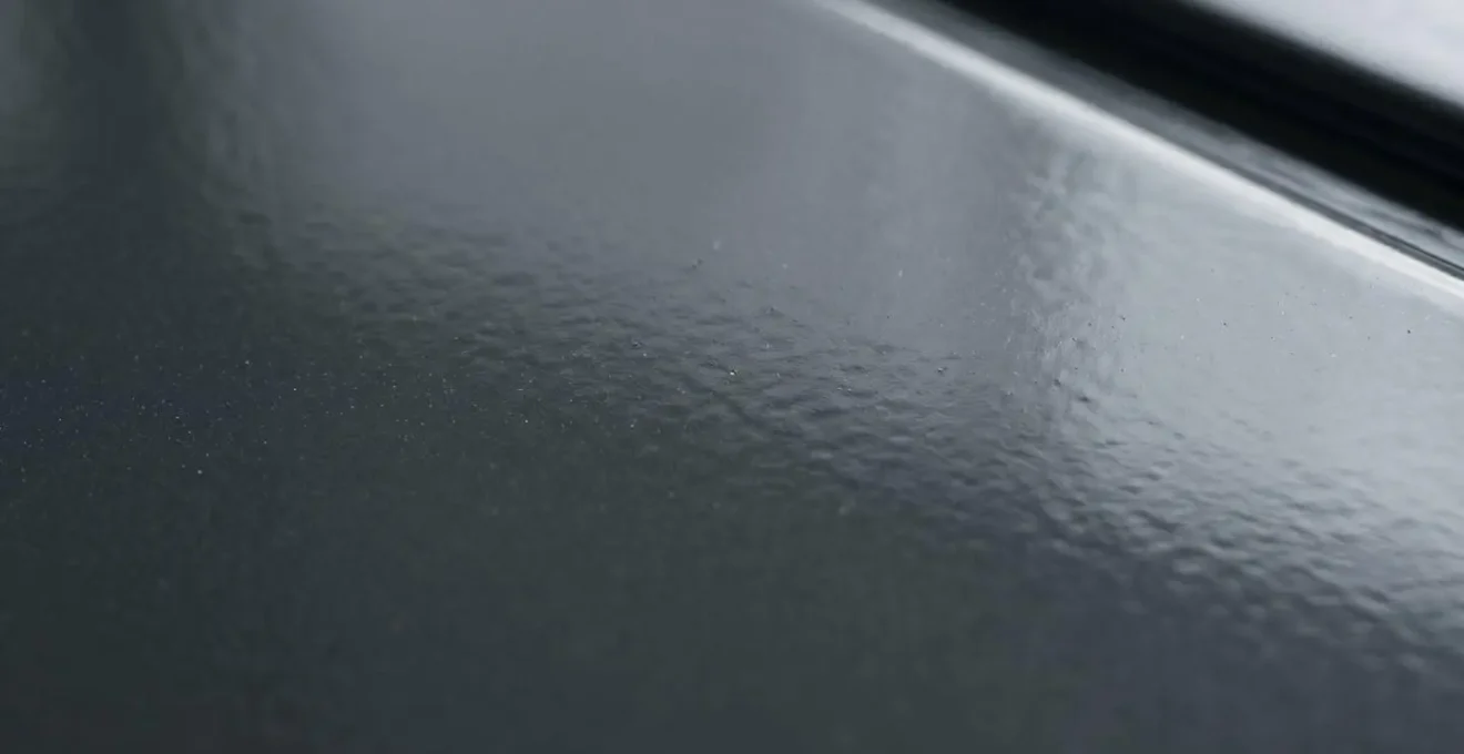 Gros plan macro surface aluminium thermolaqué anthracite RAL 7016, finition lisse brillante avec reflet lumière naturelle, uniformité couleur parfaite
