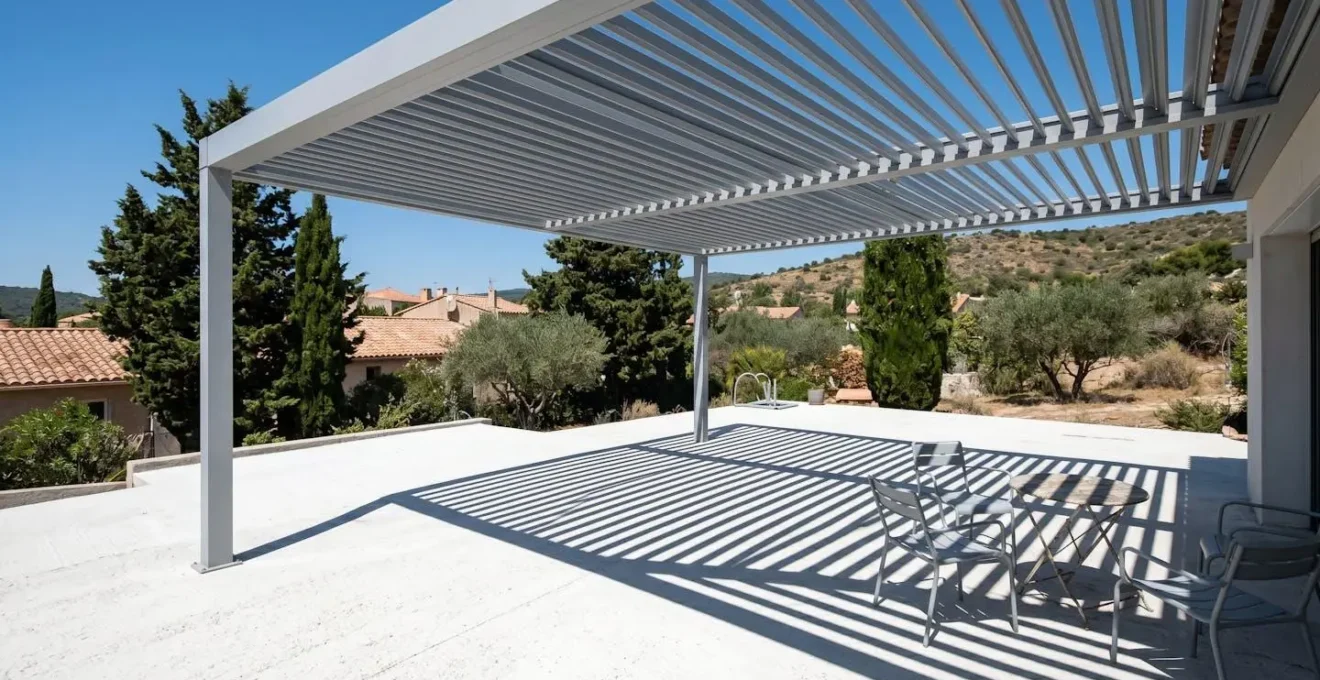 Structure pare-soleil aluminium projetant ombres géométriques nettes sur terrasse béton blanc, soleil zénithal intense, ciel bleu méditerranéen